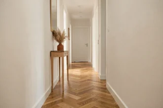 Couloir étroit aux murs blanc cassé avec parquet en chêne en chevrons et console en bois naturel, décoré d'un vase en terre cuite