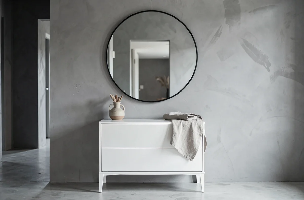 Grand miroir rond noir 80 cm centré au-dessus d'une commode blanche dans un couloir scandinave