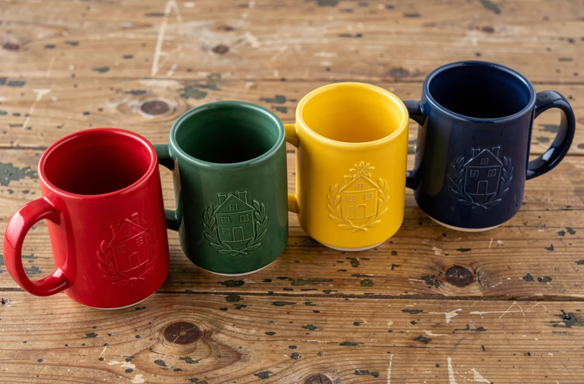 Quatre mugs en céramique colorés représentant chacun une maison différente posés sur une table en bois rustique