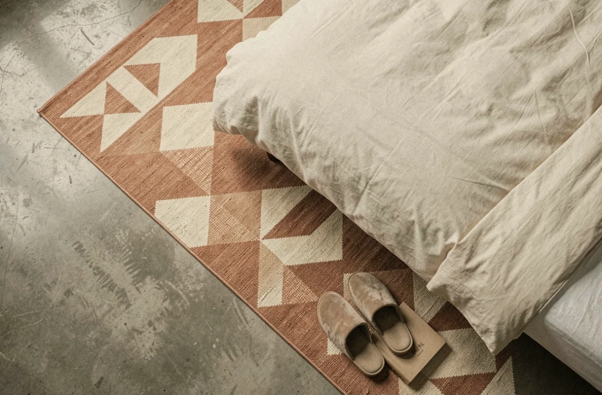 Vue de dessus d'un tapis géométrique terracotta sous un lit en béton dans une chambre urbaine
